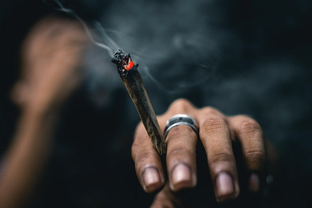 a person wearing a ring on their middle finger holding a joint or marijuana cigarette while it is burning