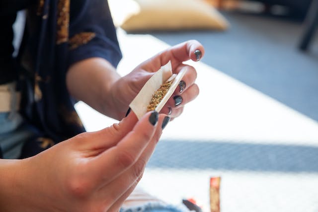 a person with painted fingernails using a rolling paper to create a marijuana cigarette also known as a joint